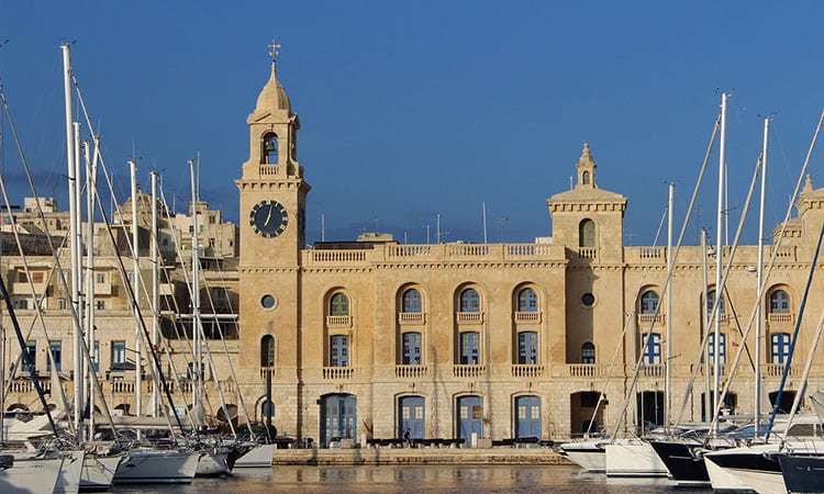 A brown building in Birgu City by the port with white boats nearby.