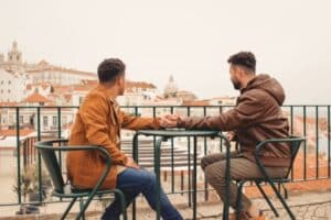 Two men holding hands while sitting at a table on a patio overlooking a city - most LGBT-friendly countries