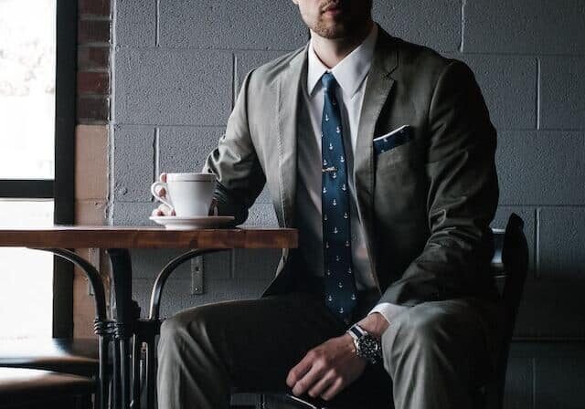 Businessman drinking coffee at a table with a gray brick wall behind him - citizenship by investment