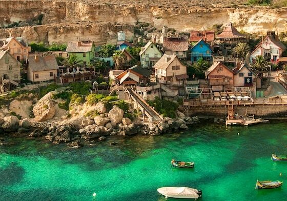 A village of houses over looking the ocean with boats nearby. 