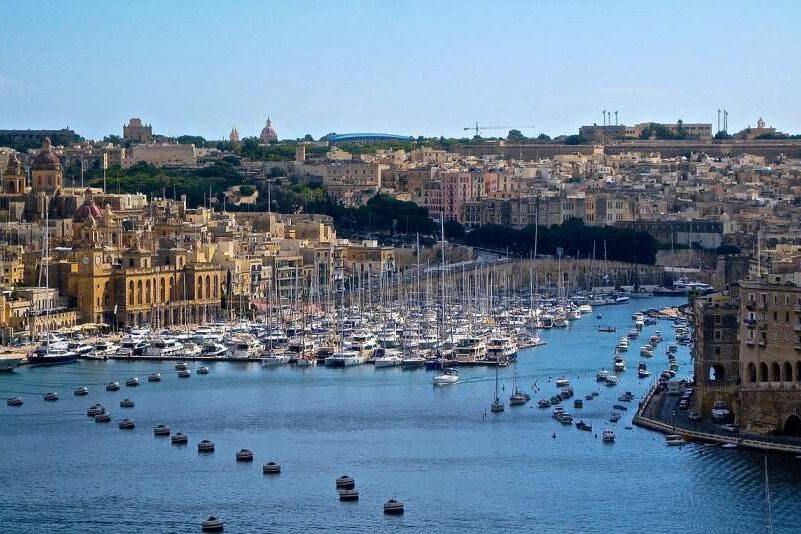 A city in Malta, with buildings around the water and boats floating nearby.