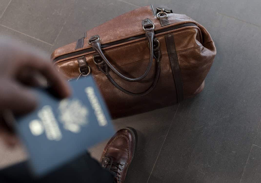 A person holding a passport and a travel bag 