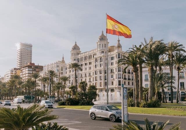 A white, government-style building in Spain, with a Spanish flag waving outside.