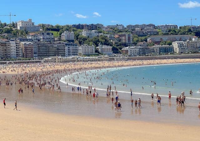 People at the beach with building in the background in San Sebastian, Spain.