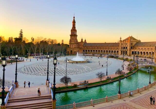 Plaza de España in Seville at sunset with a fountain and people walking around.