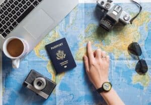 Hand pointing to a map with cameras, sunglasses and a passport laying around - passport validity and passport renewal