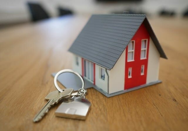 Model house on a wooden table next to a set of keys with a house-shaped keychain.