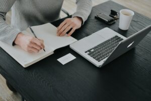 Woman writing in a notebook in front of a laptop at a desk - economic citizenship requirements