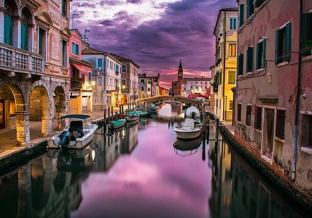  A stream of water flowing between buildings with boats in it, located in Italy