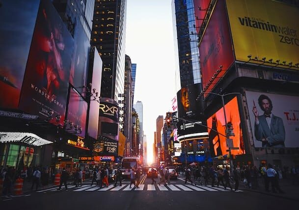 Billboards on high rises in New York near Times Square and people walking across crosswalk - wealthiest countries in the world