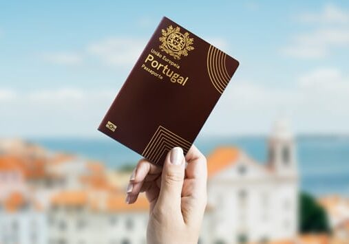 Hand holding a Portuguese passport with a scenic view of a coastal town in the background.