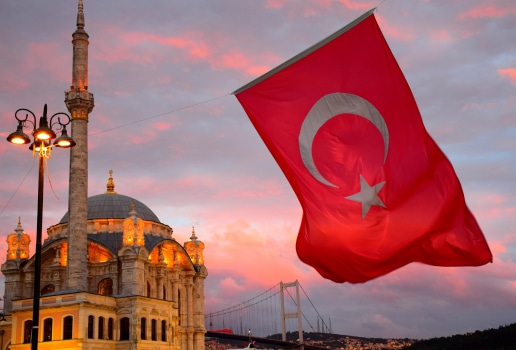 Blue Mosque of Turkey in front of a pink sunset sky with a Turkish flag in the foreground 