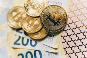 Stack of gold Bitcoin tokens placed on top of several 200 Euro banknotes.