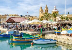View of restaurants and boats moored in the ocean on the coast of Malta - tax havens for cryptocurrency
