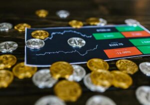 Gold and silver crypto coins scattered around a printed trading chart with price indicators on a dark table.
