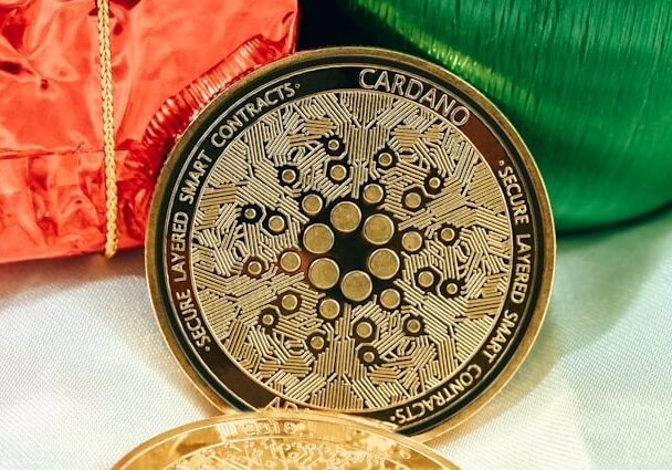 Cardano cryptocurrency coin leaning up against green and orange shiny presents - Listicle of top cryptocurrencies to invest in 