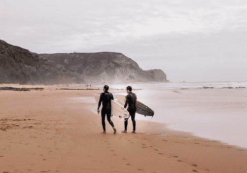 Two men with surfboards walking together on a beach - LGBT friendly country Portugal