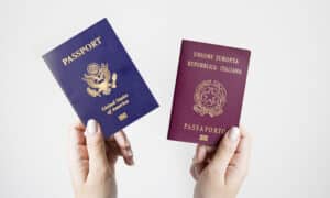 Woman's hands holding up passports against a white wall - dual citizenship