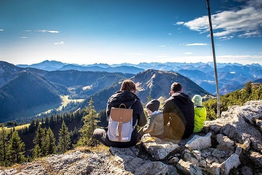 Family sitting on rocks overlooking a mountain range on a cold, sunny day - Benefits of Citizenship by Investment Programs