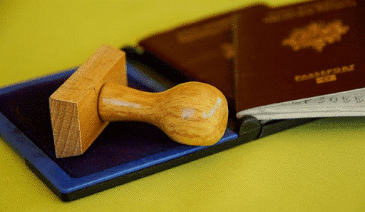 Stamp and ink next to two red passports on a yellow table - benefits of multiple citizenships