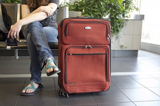 Woman sitting in an airport terminal with red luggage standing next to her - Determine your Passport needs