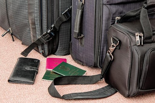 Row of black luggage bags standing on the floor with a wallet and passports laying next to it - multiple passports for portfolio diversification