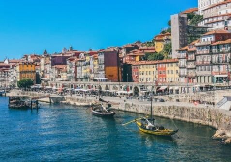 Colorful buildings line the Douro River waterfront in Porto, Portugal, with traditional boats docked.