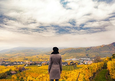 Woman looking over yellow and red autumnal fields in Austria on a partly cloudy day - safe woman-friendly countries in the world