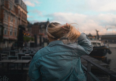 View from behind of a woman wearing a denim jacket and pulling on her blonde hair while walking in Belgium - European countries that are safest for women