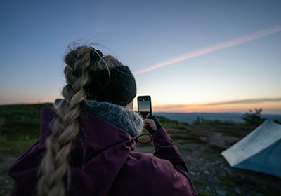 Woman taking a picture of the sunset while camping in Finland - safe female-friendly countries