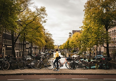 Woman with a black beanie and yellow jacket walking next to bicycles in Netherlands - safest countries in the world for women