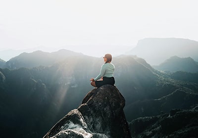 Woman meditating on a hilltop with sun rays shining on her in New Zealand - safe places for women