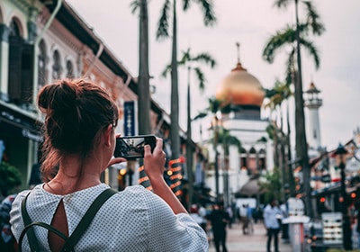 Woman wearing a white blouse and black backpack taking photos while visiting Singapore - Asian country safe for women