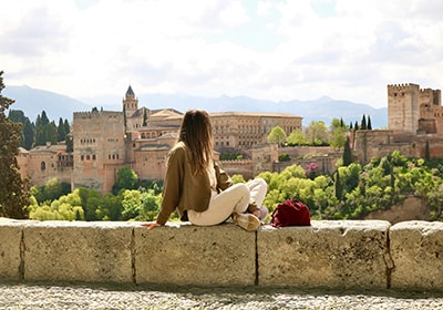 Woman sitting on a wall, looking out over Alhambra in Spain - determining your country of residence as an immigrant