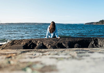 Woman sitting on the rocks, looking out over the ocean in Sweden - safe country for women to travel or live in alone