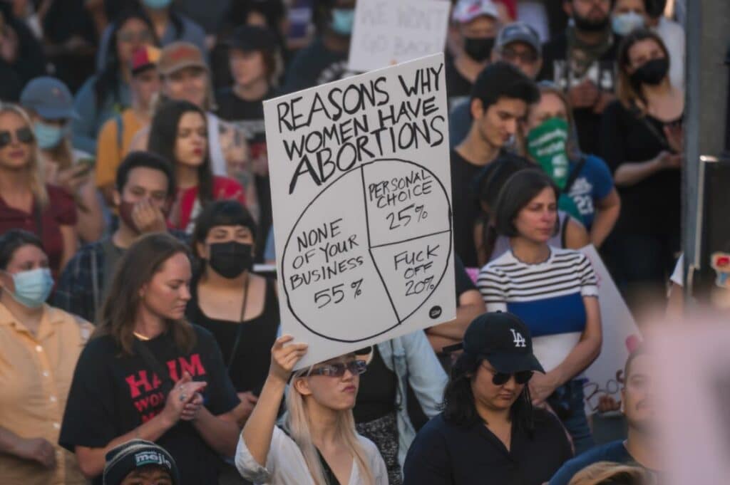 Woman holding a sign saying "Reasons Why Women Have Abortions" listing three public opinions