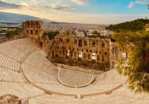 Ancient stone theater in Athens, Greece, with city buildings in the background.