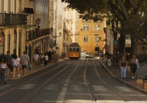 Tram in Portuguese street lined with trees and people walking alongside - Portugal Golden Visa