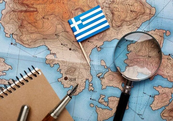 Living in Greece map of the world with greek flag and a magnifying glass