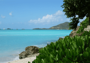 a view from a beach of blue ocean water and mountains in antigua
