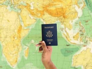 Hand holding up a passport in front of world map - Benefits of dual citizenship