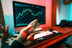 A person holding a bitcoin with a computer in the background. 