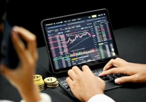 Person analyzing cryptocurrency trading charts on a tablet with stacked Bitcoin tokens nearby.