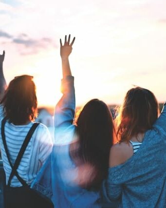 People from behind standing in front of sunset raising their hands up in the air - best work and living places