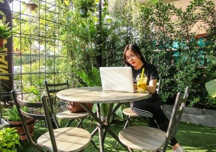Woman sitting at a desk in a greenhouse with a laptop and smoothie in front of her - European digital nomad visas