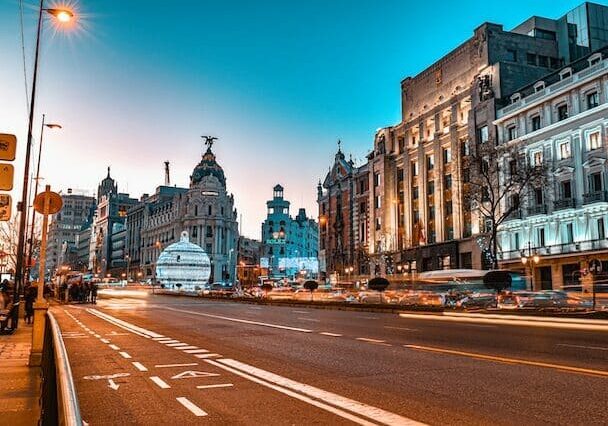 Street view of Madrid at sunset with historic buildings and light trails from cars.