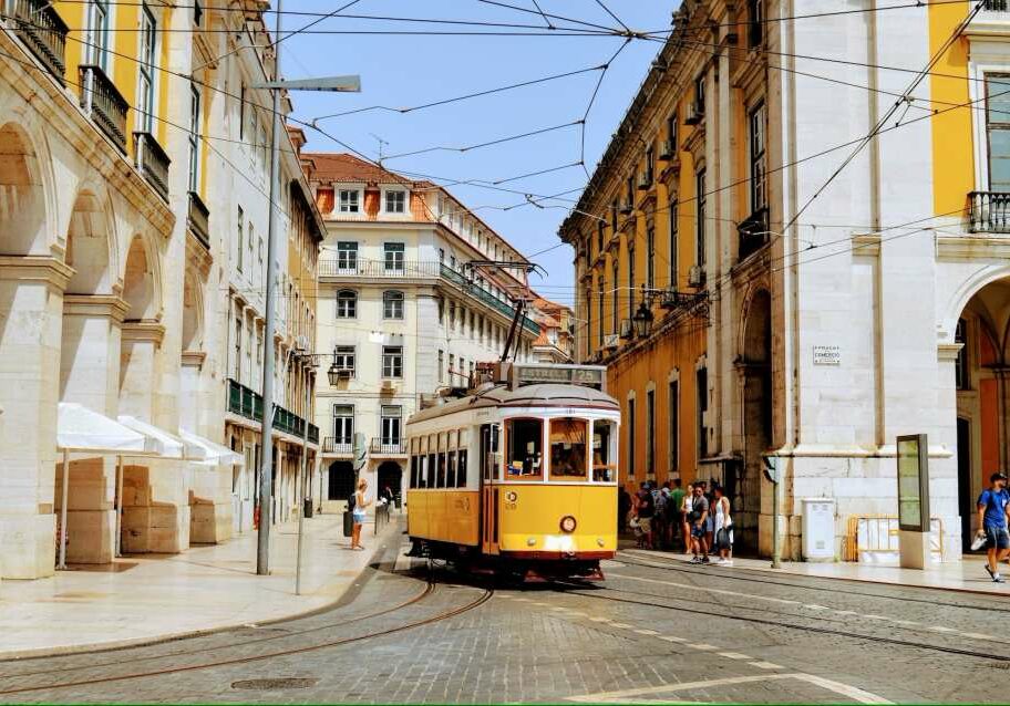 Iconic yellow tram surrounded by classic Portuguese buildings and people walking in the street - Best European Countries to Live in for Expats