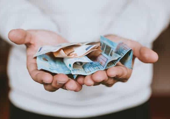 Two hands holding out a bunch of money notes - donating to charity to avoid paying taxes legally