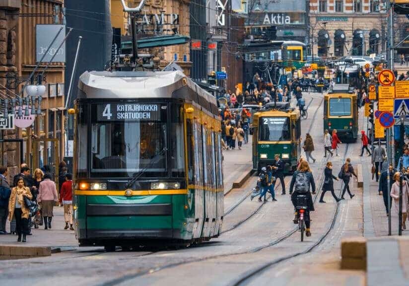 Green and yellow trams in Finland with people walking and cycling alongside the tracks - expat-friendly best countries to live in