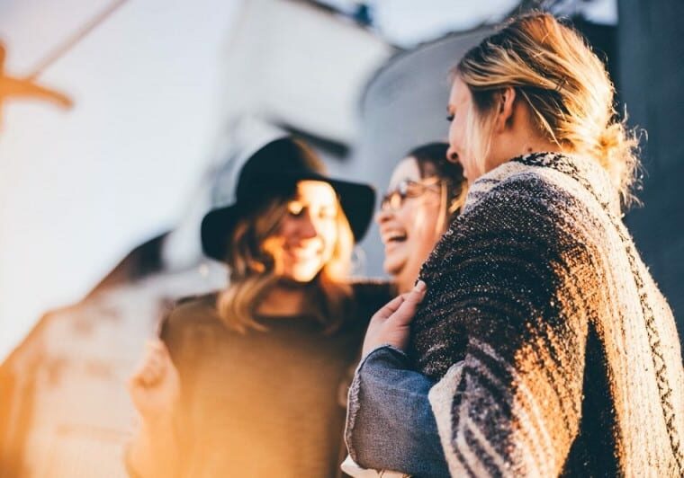 Three women standing next to each other, laughing - richest countries according to World Happiness Report